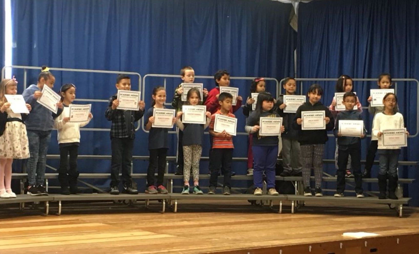 Group of children standing on a stage holding certificates