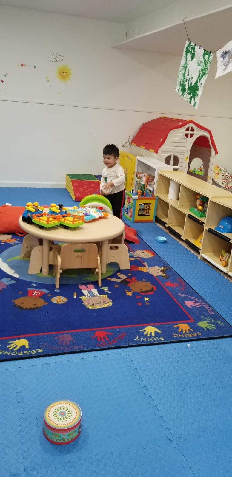 Child standing in a playroom with a small table and toys