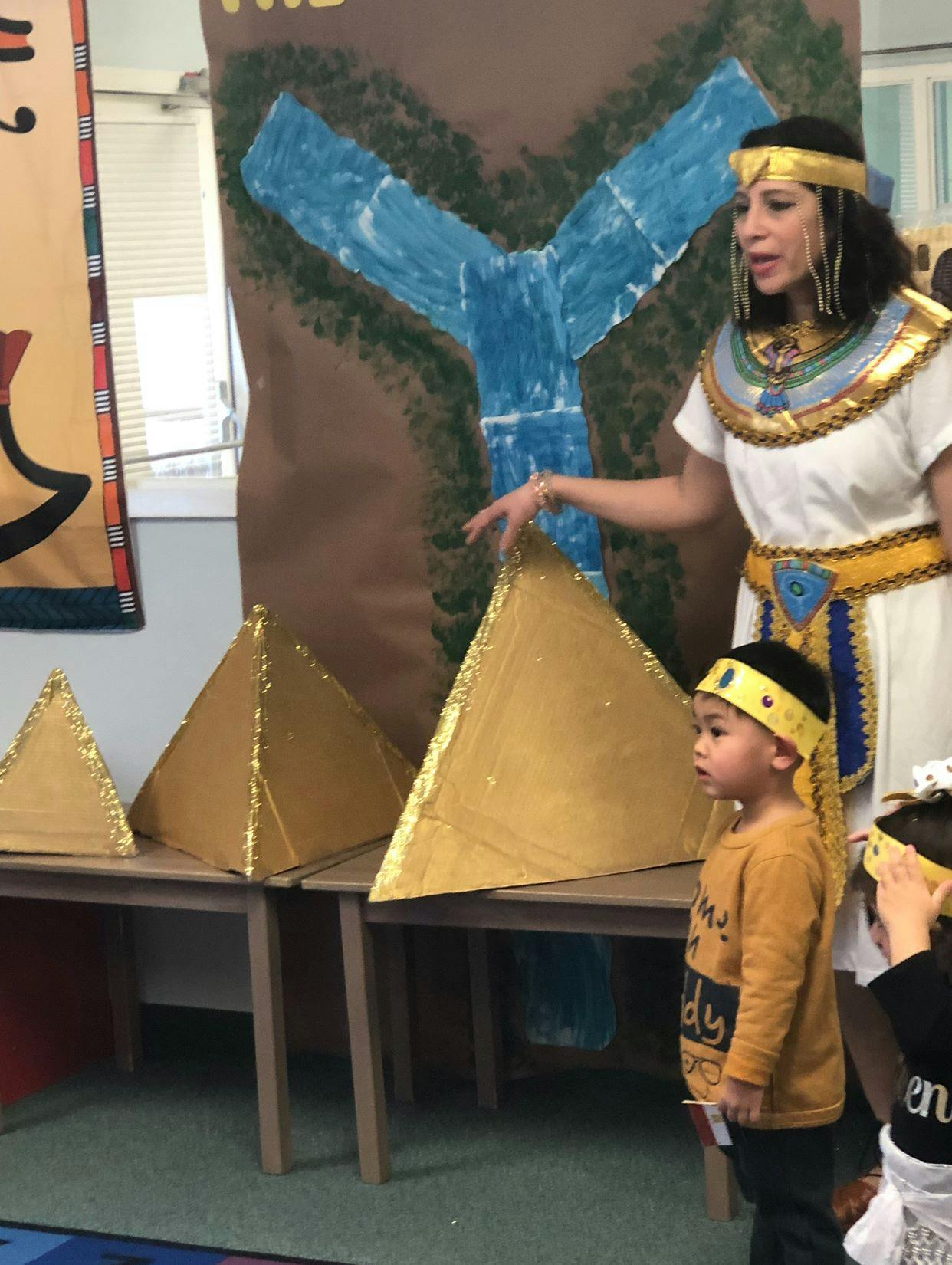 Person in costume pointing at pyramids with a child watching