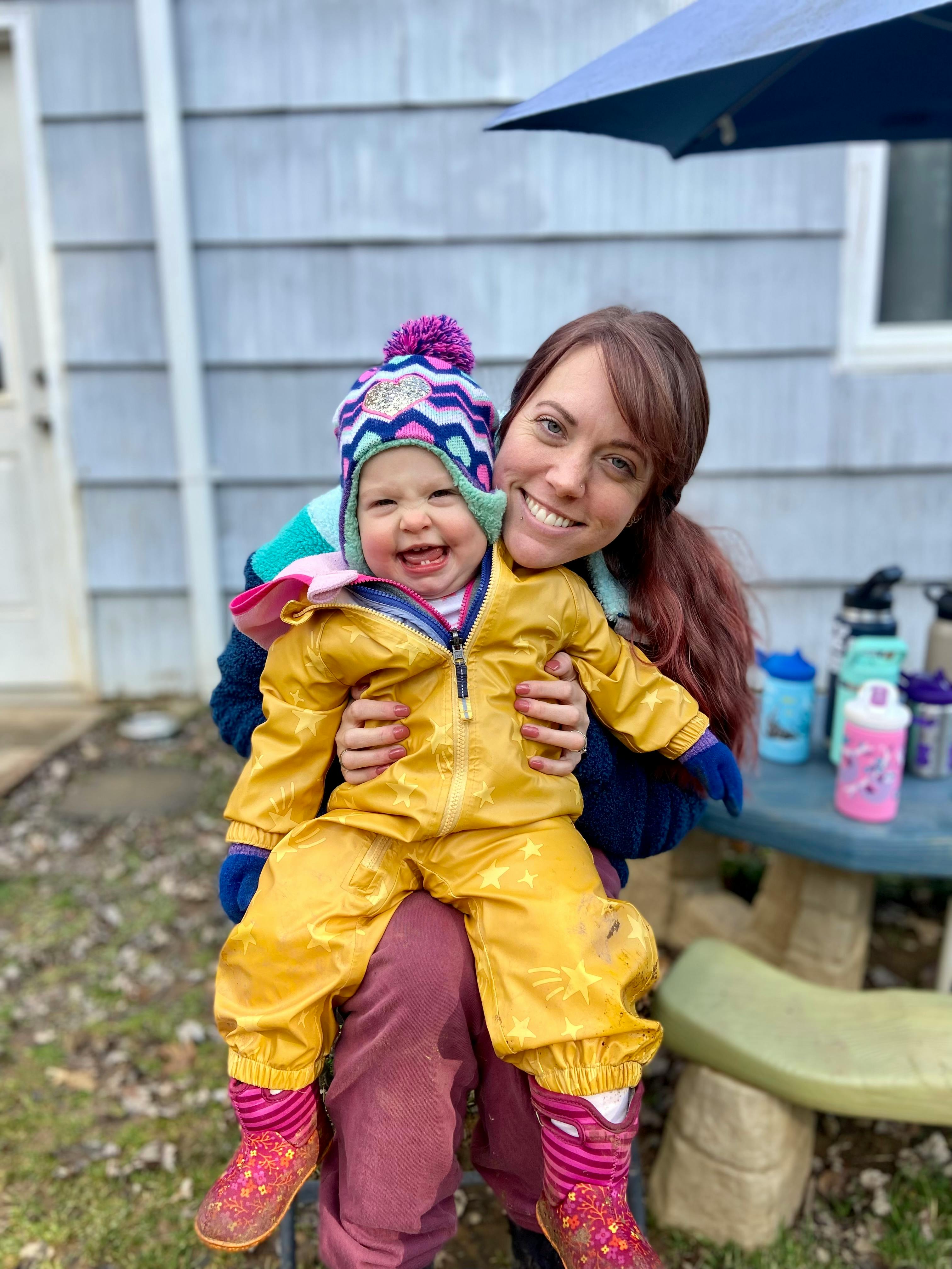 Person holding a child wearing a yellow snowsuit and a colorful hat