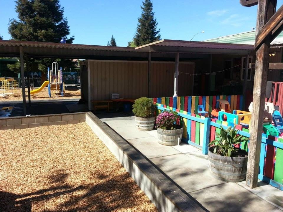 Outdoor playground area with wood chips and a colorful fence