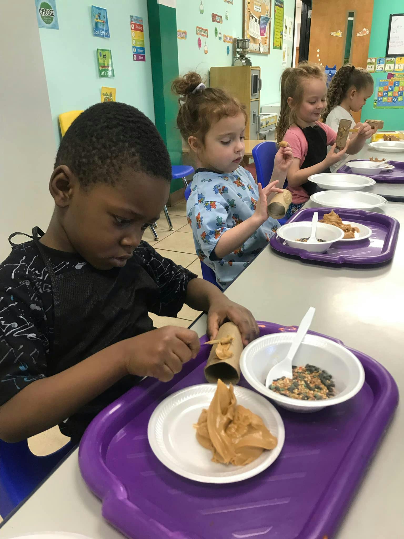 Child making a craft with a cardboard tube and peanut butter in a classroom