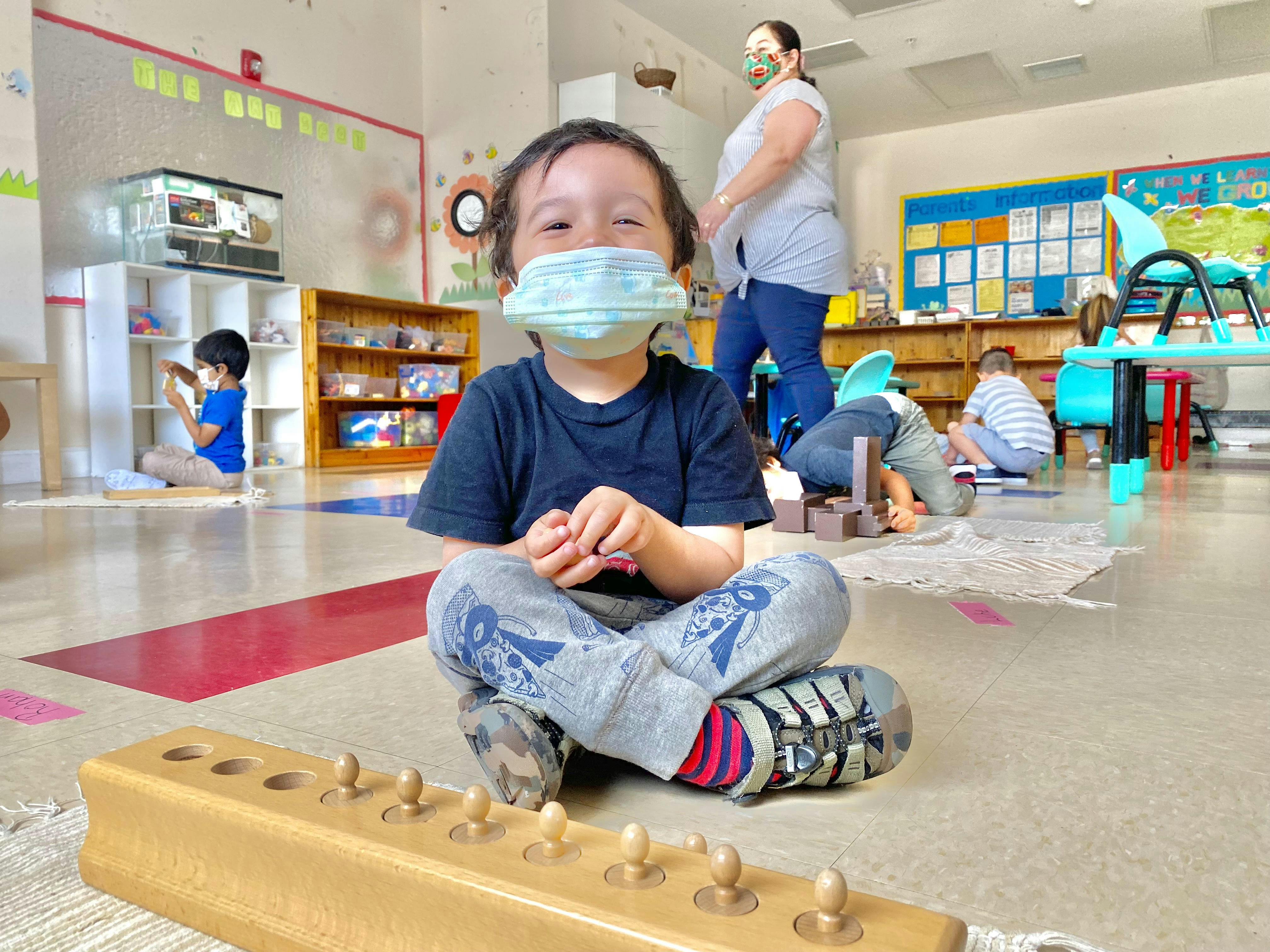 Child in a mask sitting on the floor in a classroom