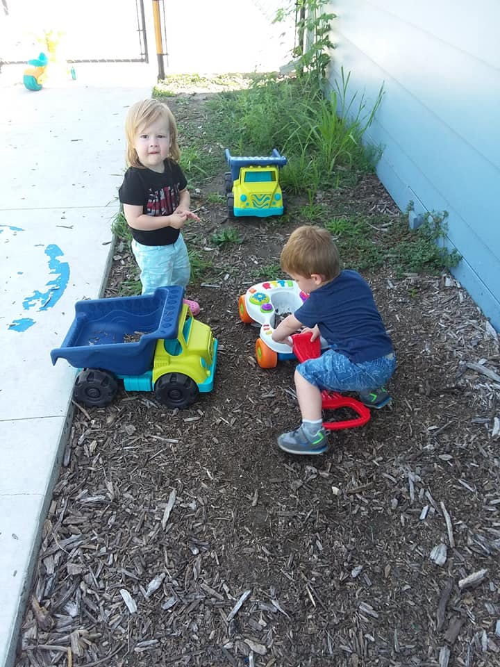 Two children playing with toys on wood chips