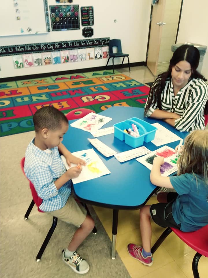 Person and two children drawing at a table in a classroom