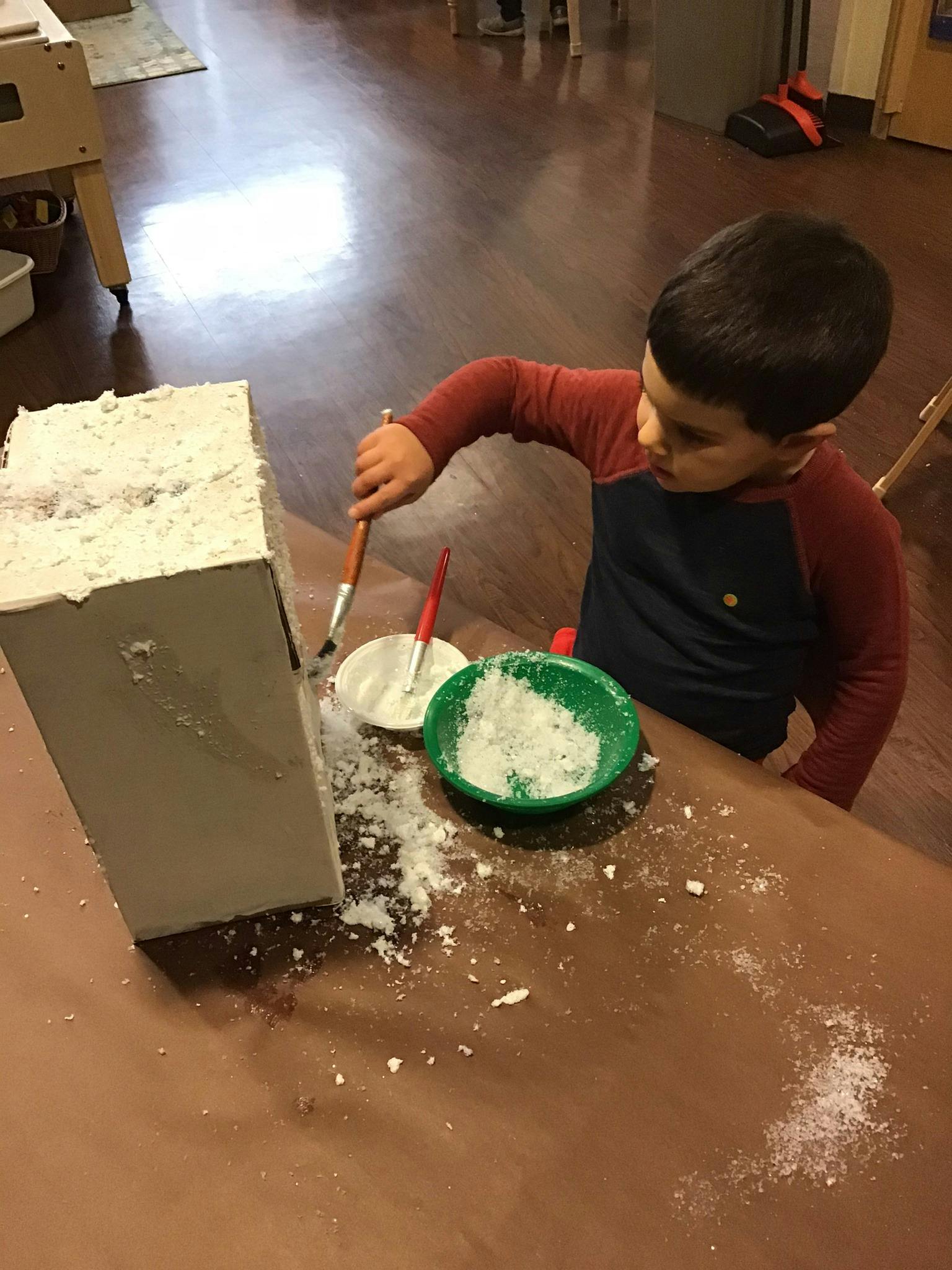 Child painting a white block with a brush and white powder