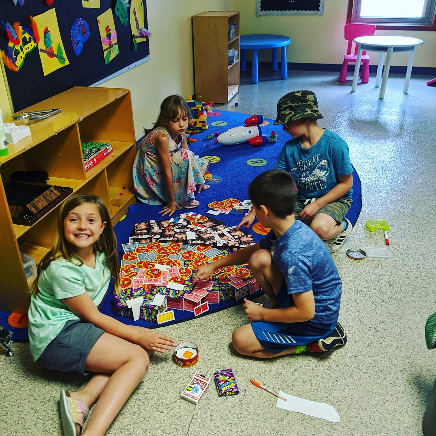 Four children playing a game on a blue mat in a classroom