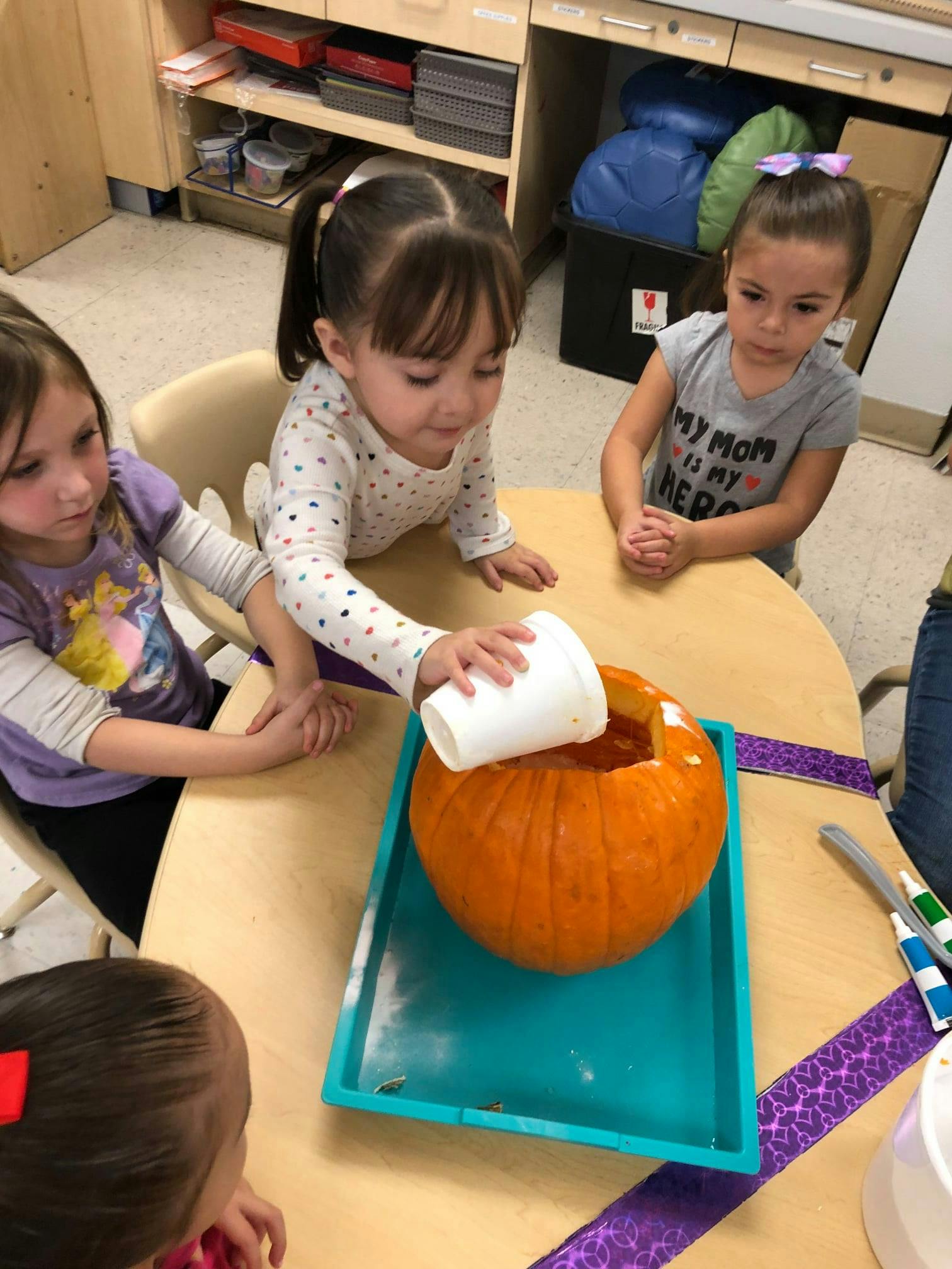 Child scooping contents from a pumpkin with a cup in a classroom