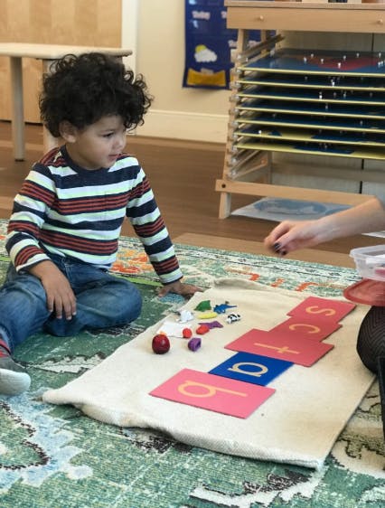 Child on floor with letter cards and small objects