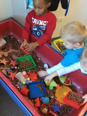 Children playing in a sensory bin with small objects and scoops