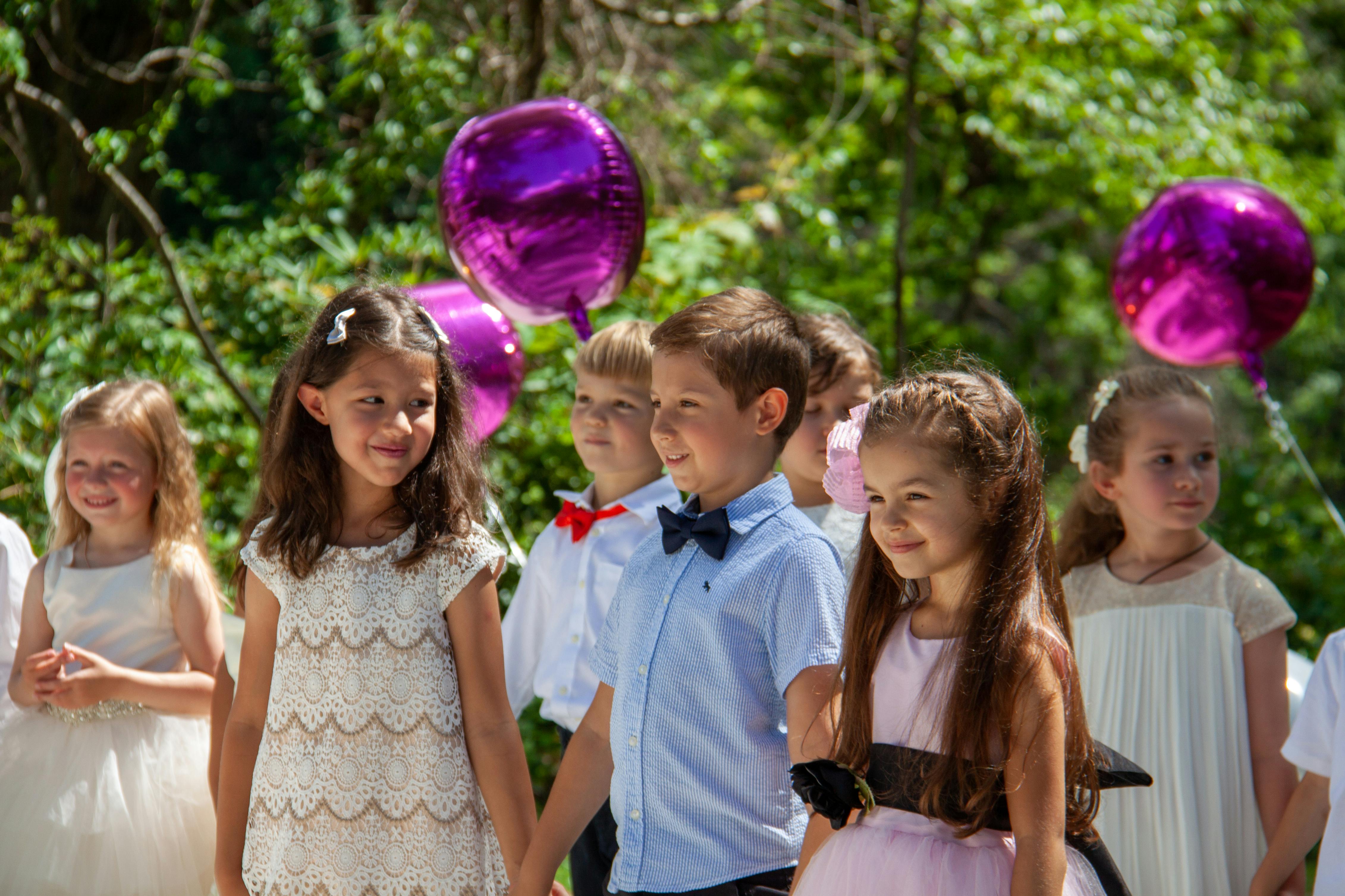 Children in formal attire holding hands with purple balloons