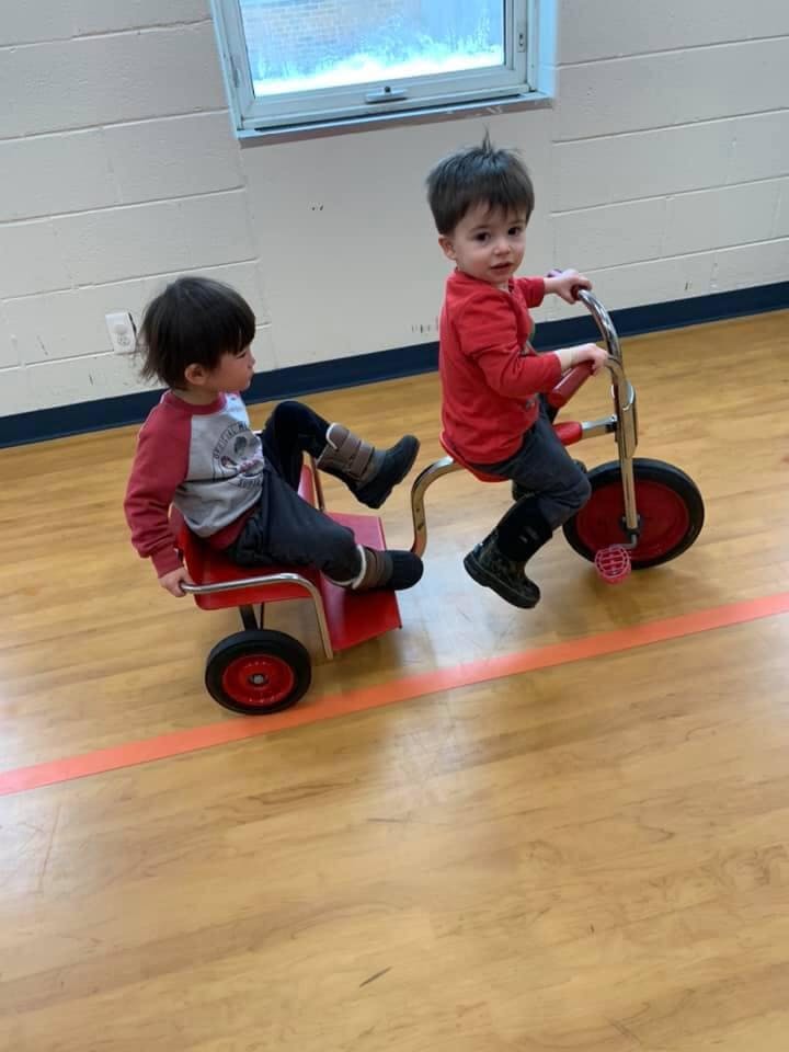 Two children playing with a tricycle and a wagon