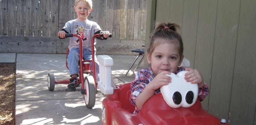 Child on a red tricycle and a child in a red toy car