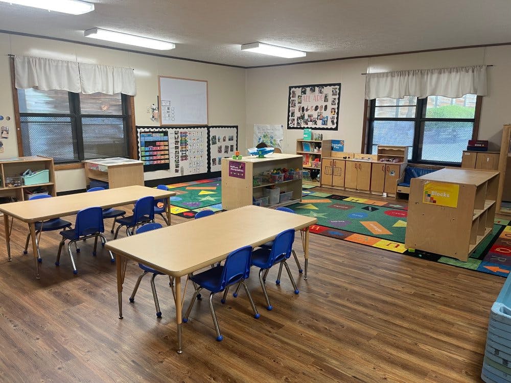 Empty classroom with small tables, blue chairs, and a colorful alphabet rug