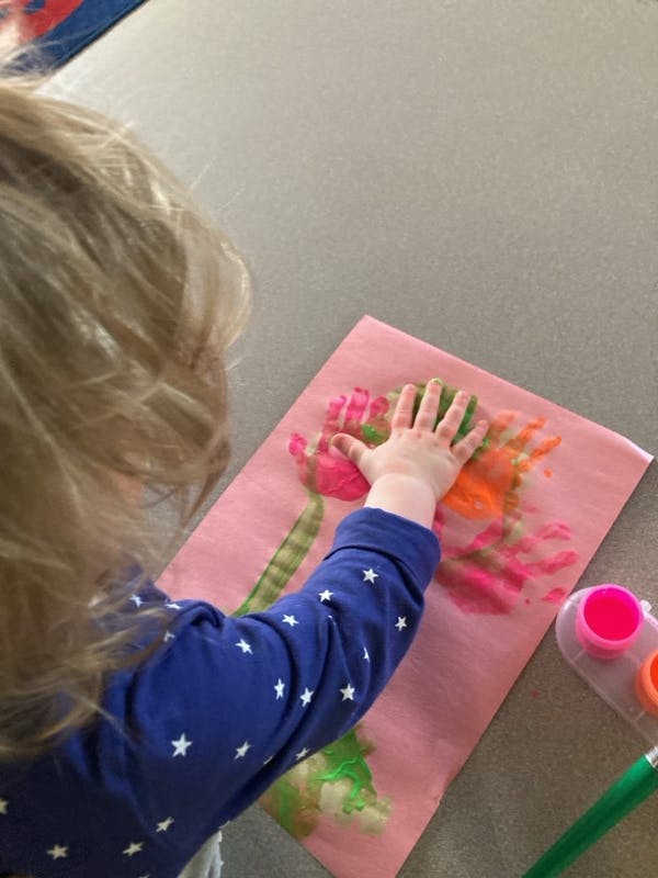 Child making a handprint painting on pink paper