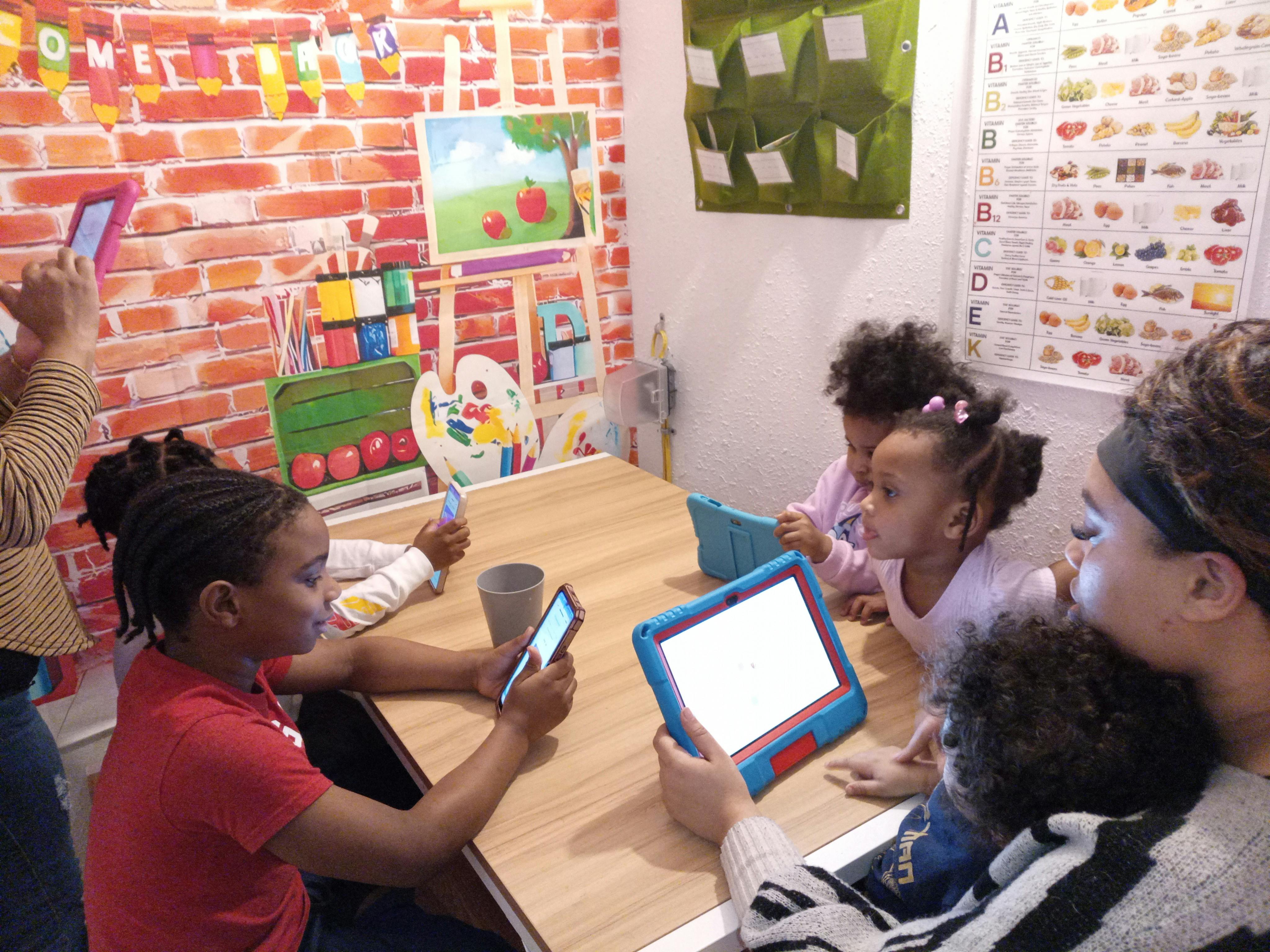 People and children gathered around a table using various tablets and phones