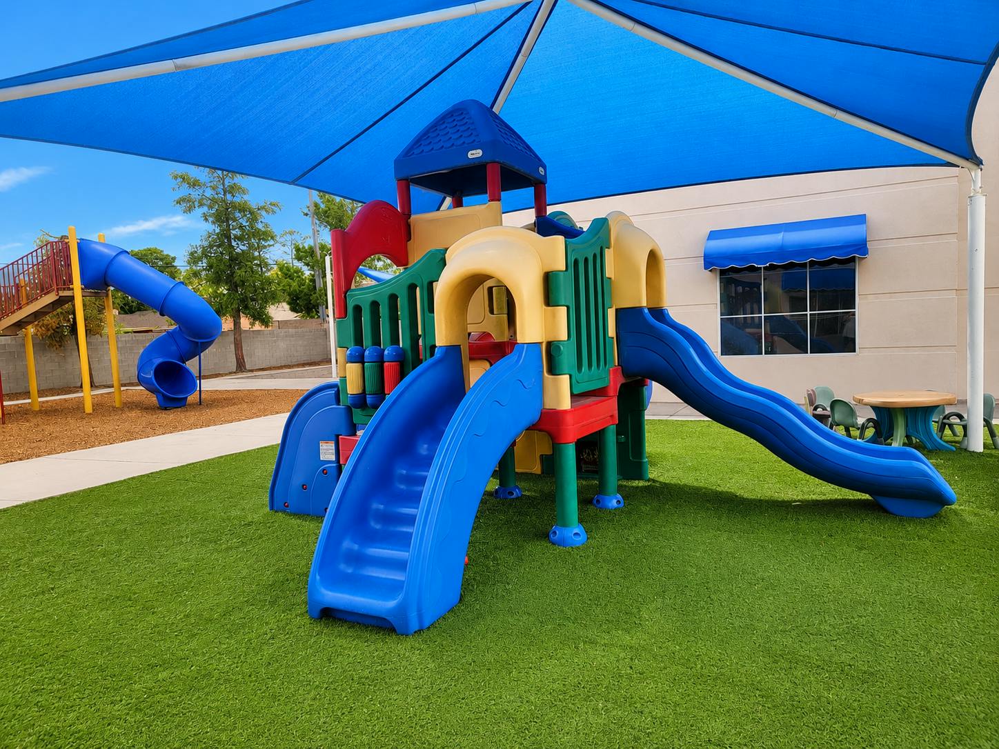 Colorful plastic playground structure with slides under a blue shade canopy