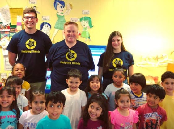 Three adults and many children posing for a group photo in a classroom