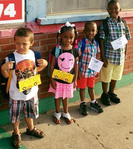 Four children standing with backpacks and school bus cutouts