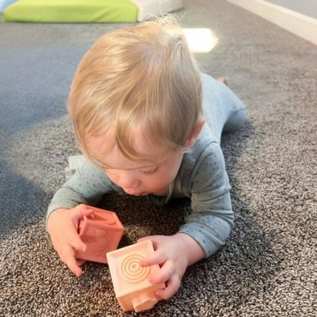 Child playing with two blocks on a carpeted floor