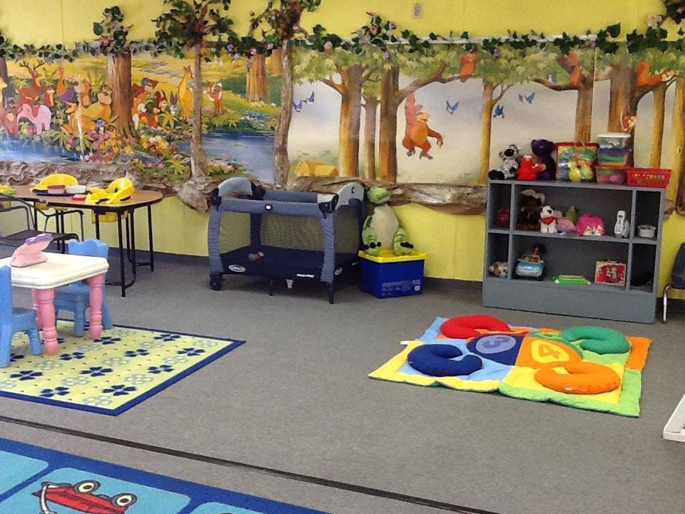 Playroom with colorful rugs, small tables, and a mural of stuffed animals