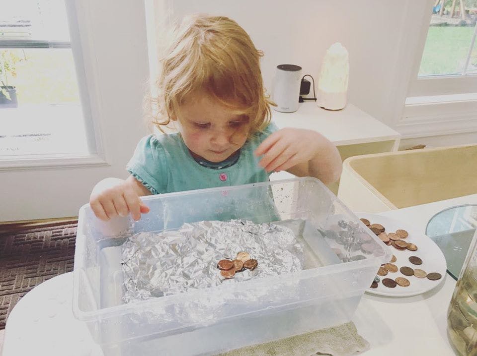 Child playing with coins in a container of water and aluminum foil