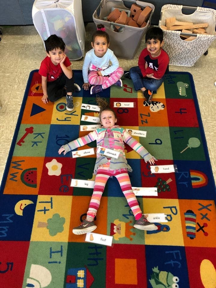 Three children on a colorful alphabet rug, one child lying down with labels