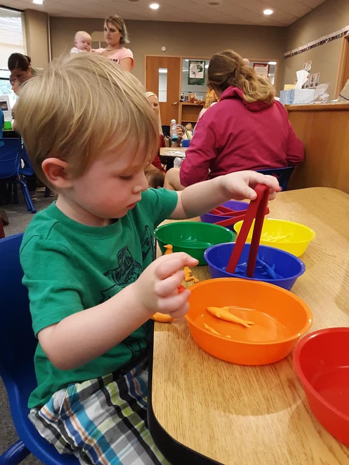 Child playing with colorful bowls and tongs at a table