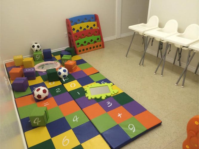 Playroom with colorful floor mats, blocks, soccer balls, and high chairs