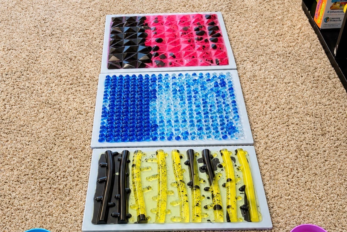 Three rectangular sensory trays with geometric plastic shapes on a carpet