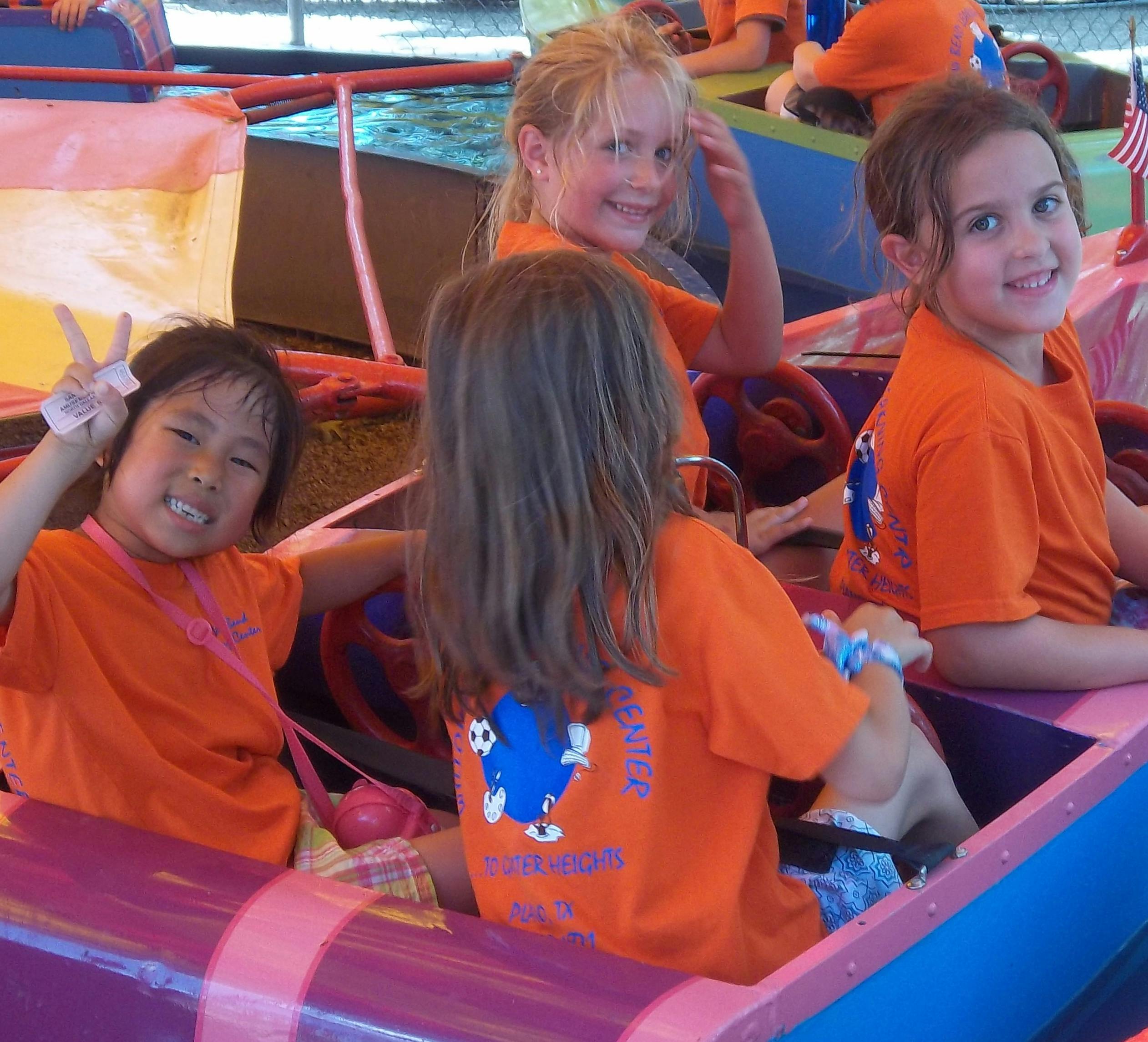 Three children in orange shirts on an amusement park ride