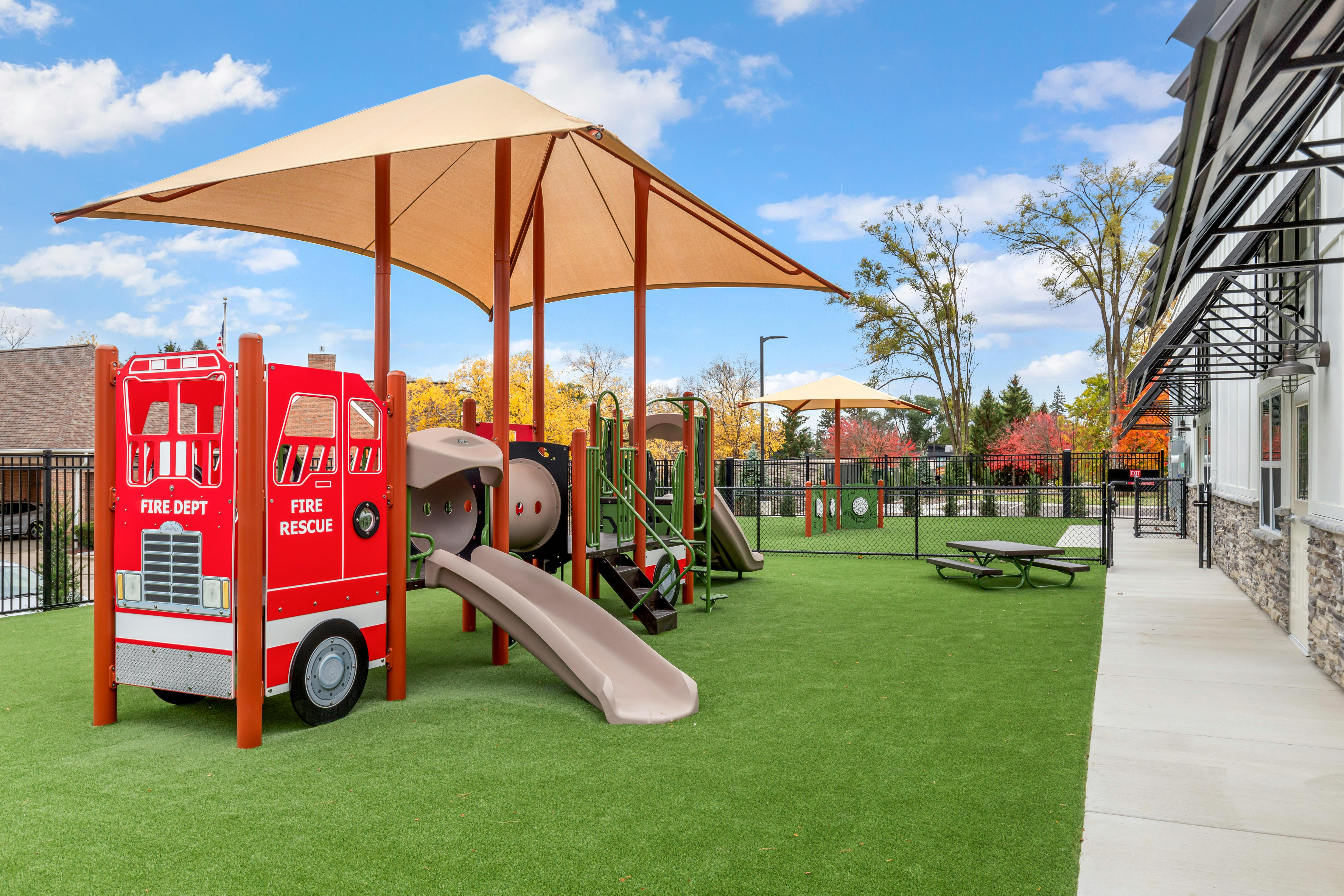 Playground with fire truck climbing structure, slides, and shaded areas