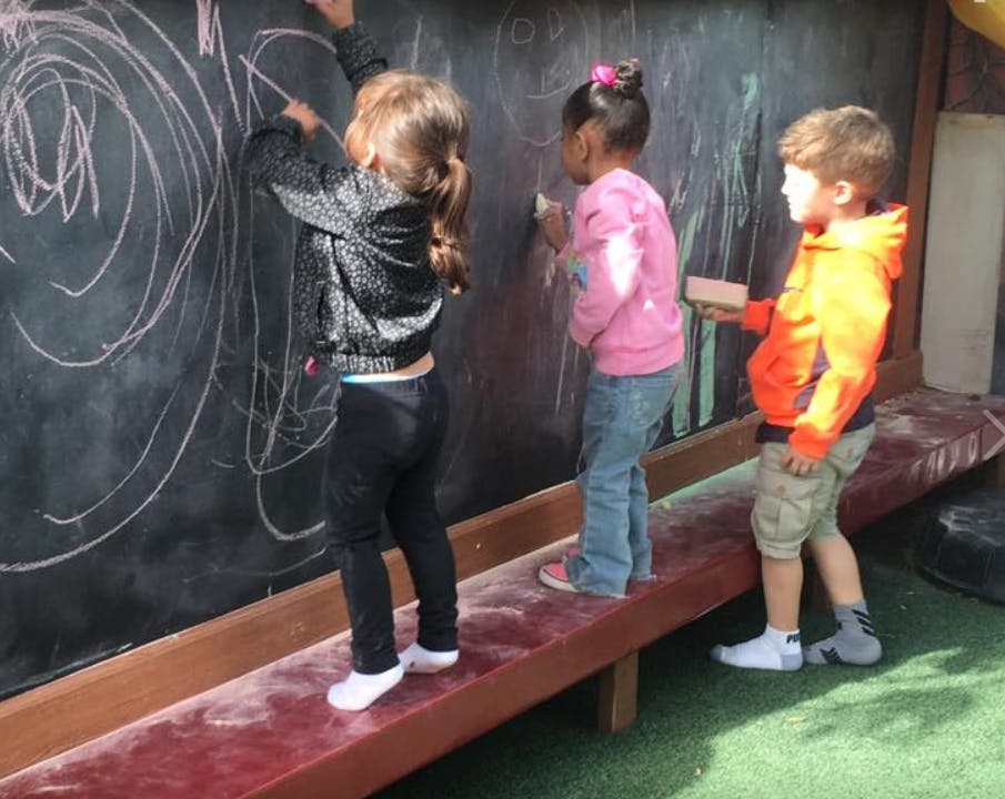 Three children drawing on a large chalkboard