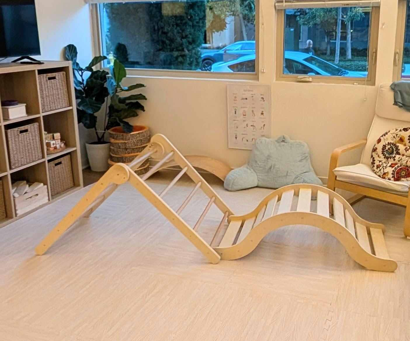 Wooden climbing structure with a ladder and wavy slide in a room