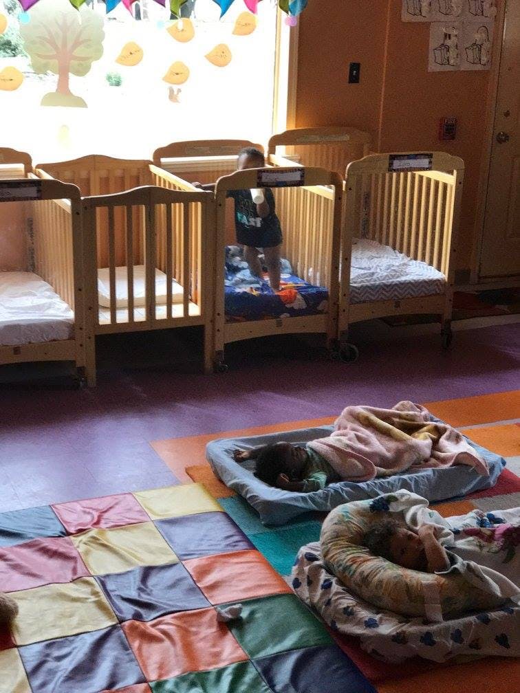 Child standing in a crib while another child sleeps on a mat