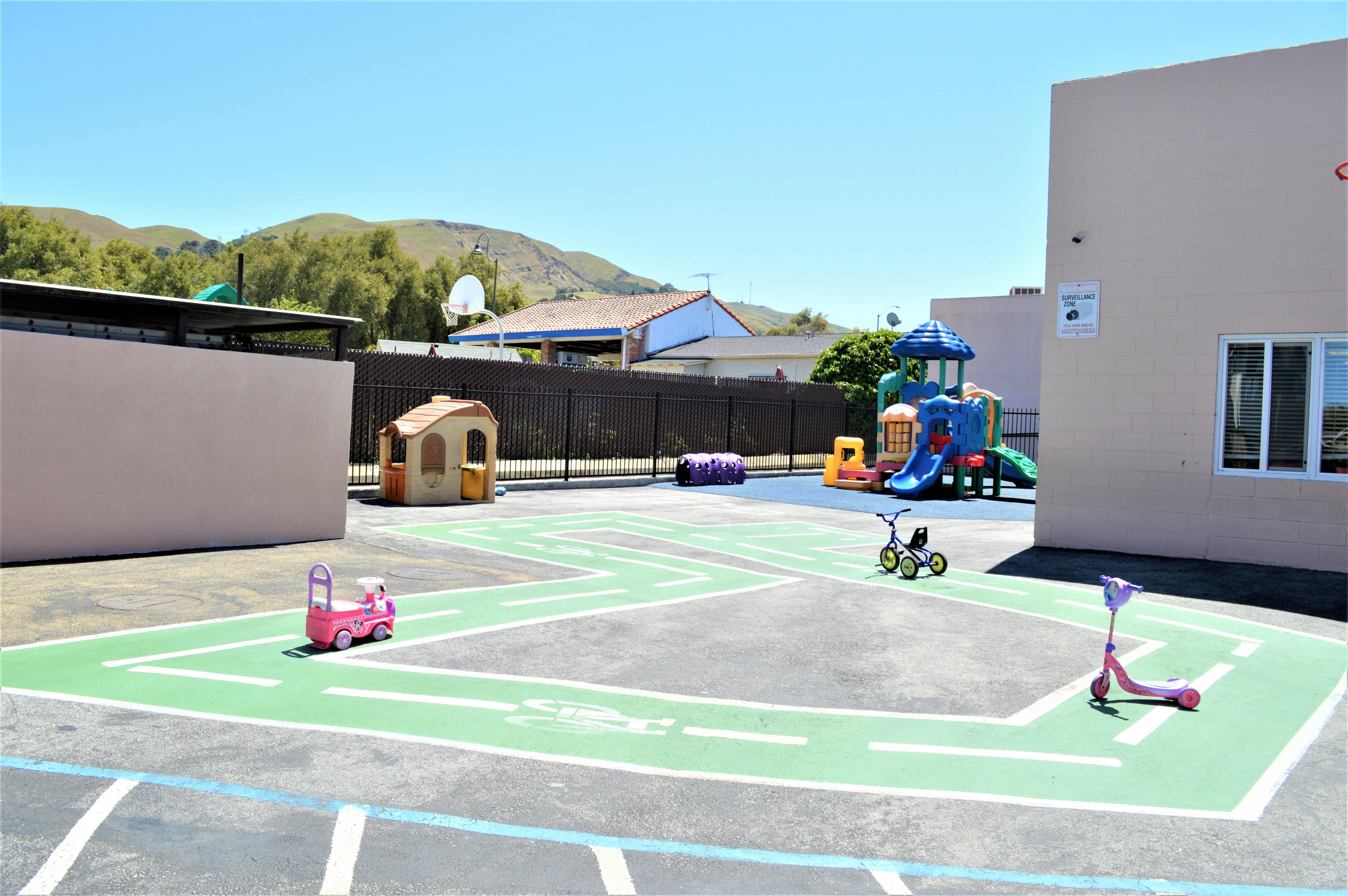 Outdoor playground with painted road on asphalt, play structure, and toy vehicles