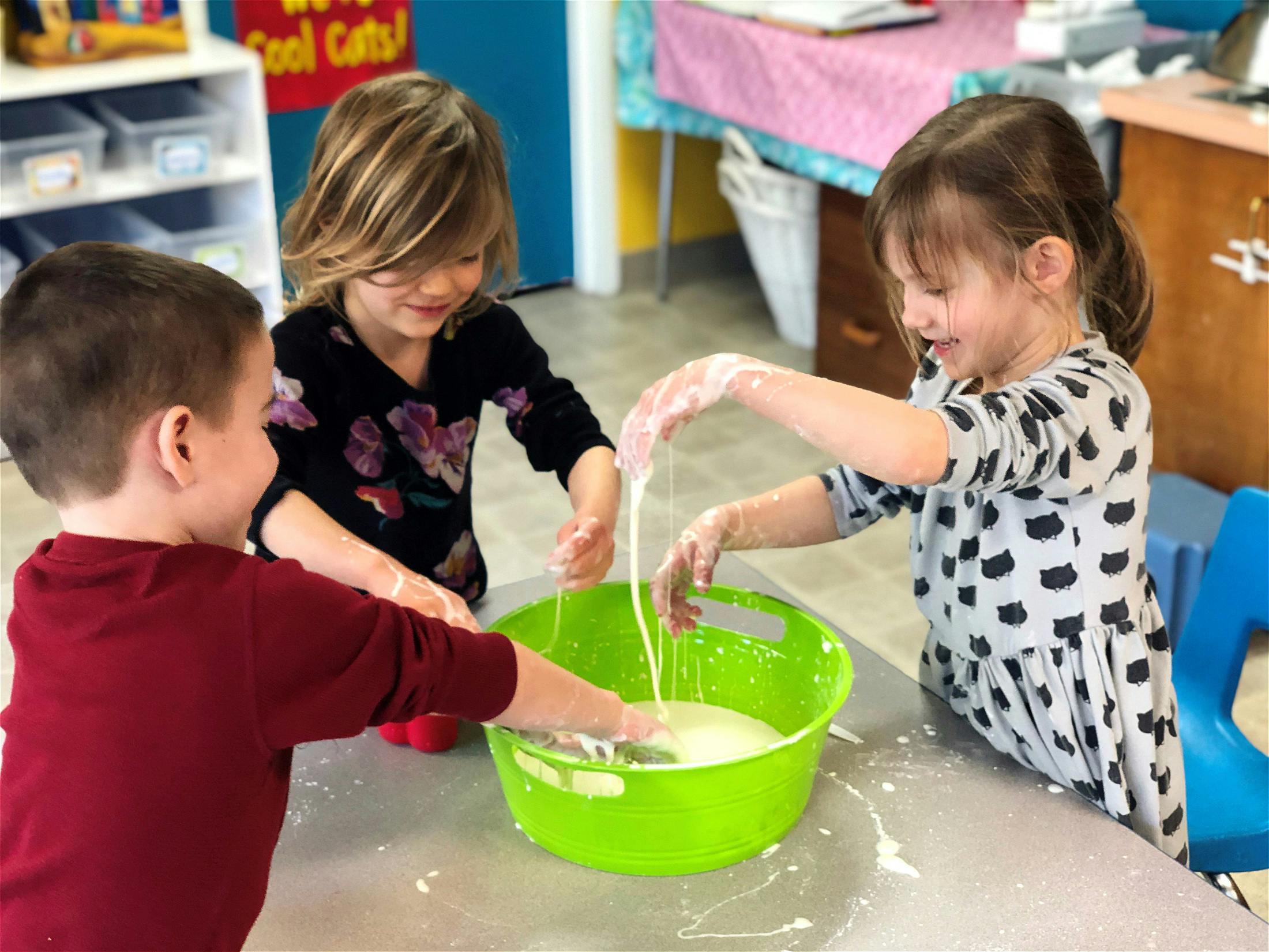 Three children playing with a green bowl of liquid