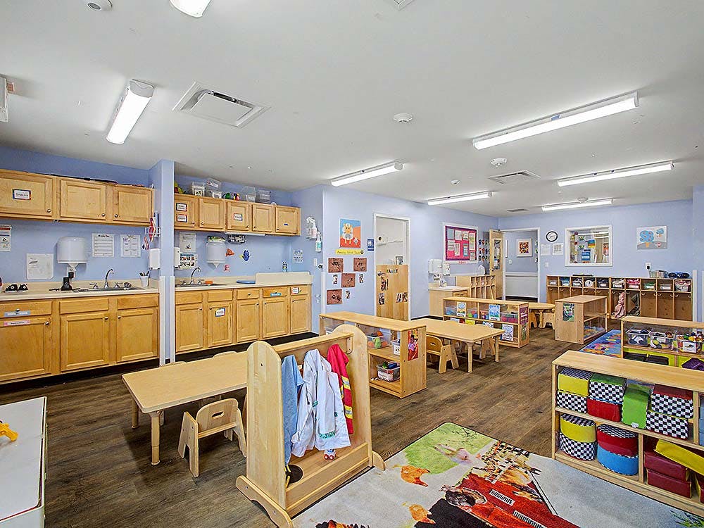 Classroom with wooden tables, chairs, cabinets, and play areas