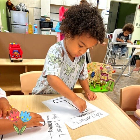 Child tracing the letter L on a worksheet at a table