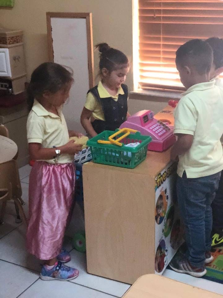 Three children playing with a toy cash register and shopping basket