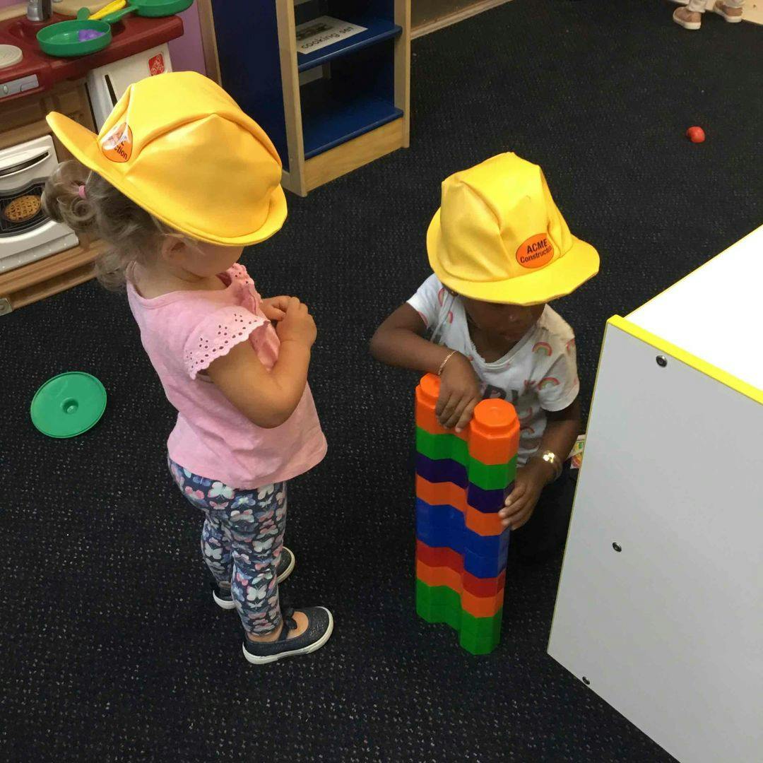 Two children in yellow hats playing with colorful blocks