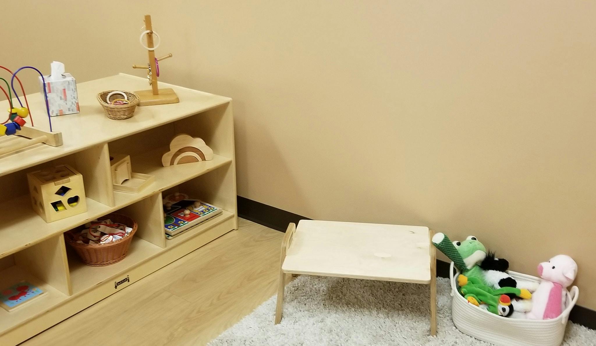 Wooden shelving unit with toys, small table, and basket of stuffed animals
