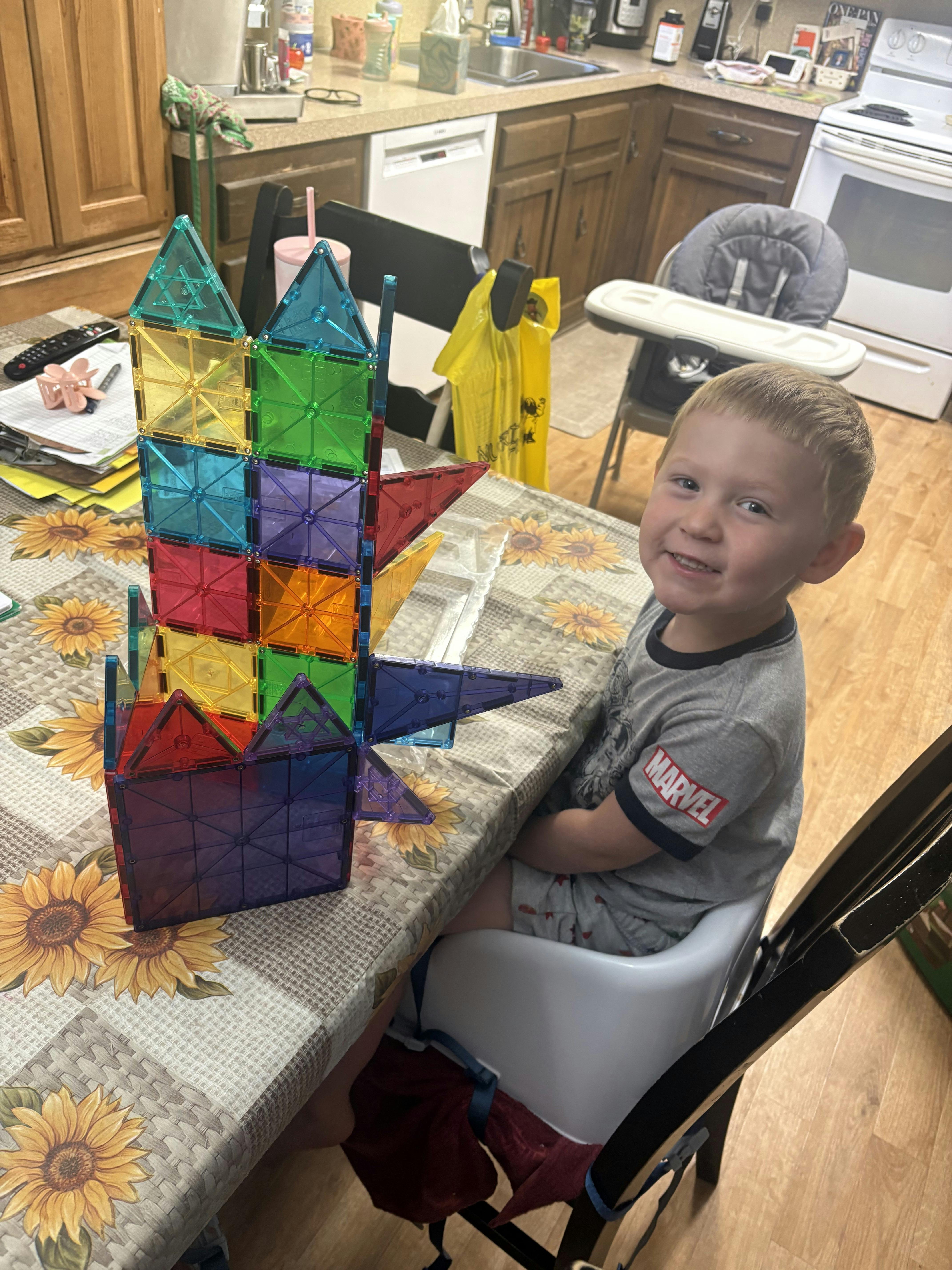 Child sitting at a kitchen table playing with colorful magnetic building tiles