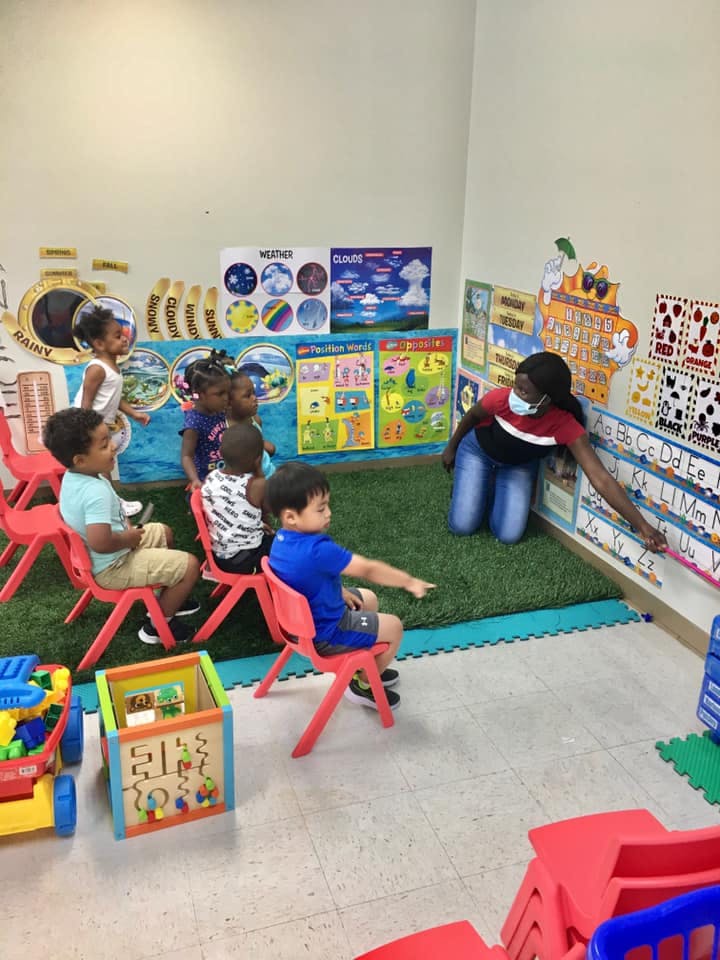 Adult and children in a classroom, adult pointing to letters on a wall