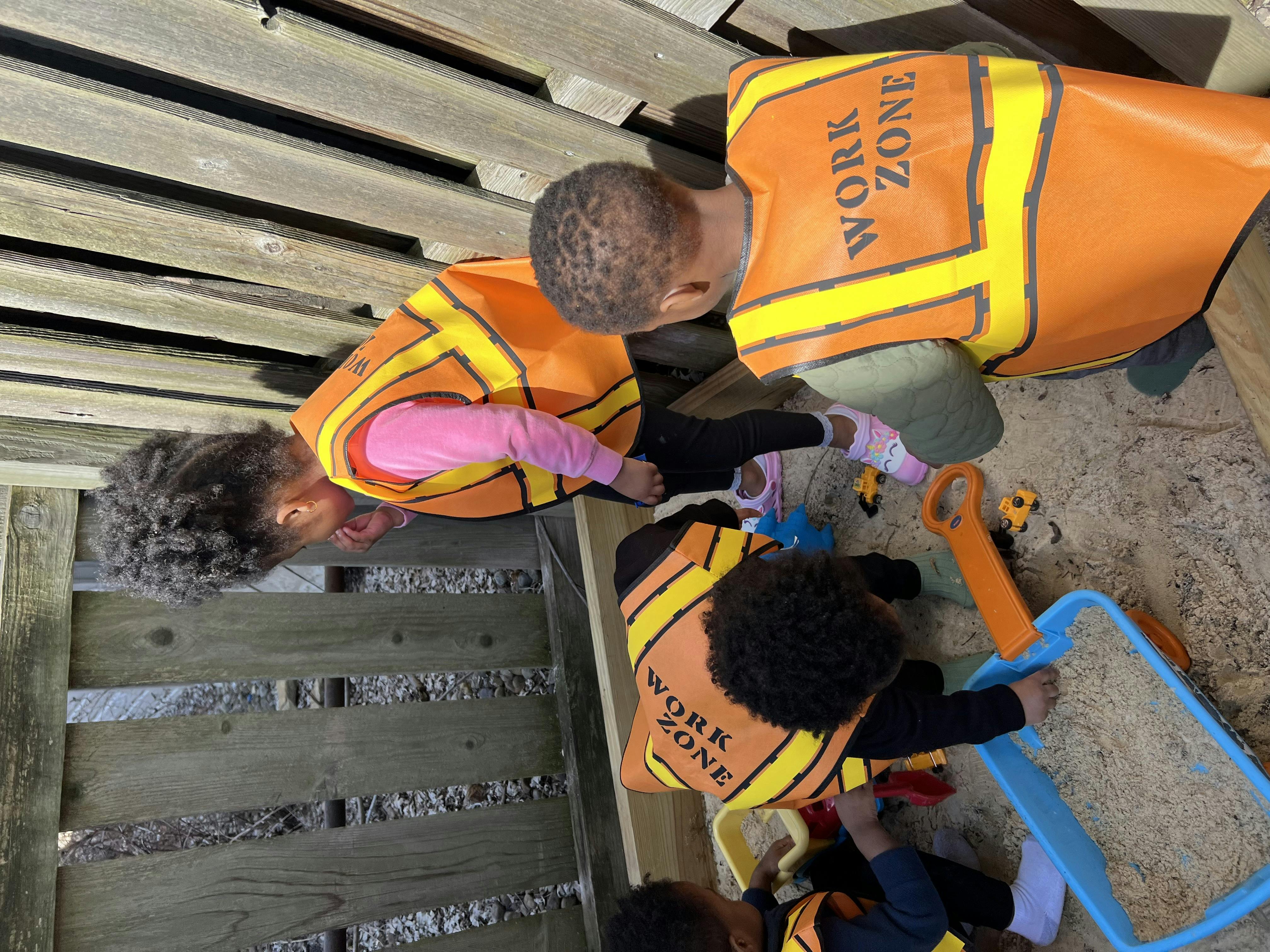 Children in work zone vests playing with sand and toys