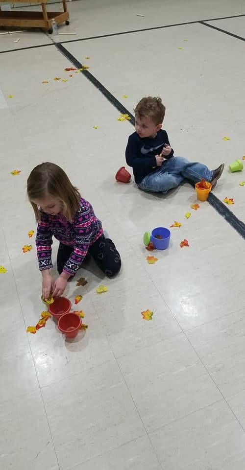 Two children playing on the floor with small colorful objects and leaf-shaped objects
