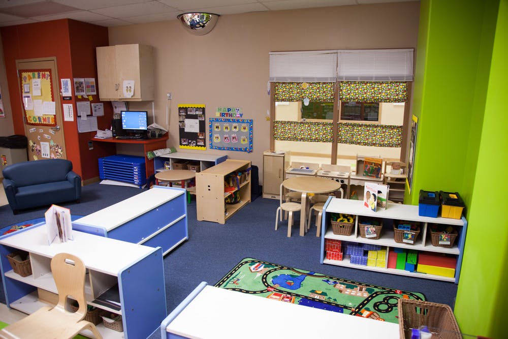 Classroom with small tables, chairs, shelves, and a computer desk