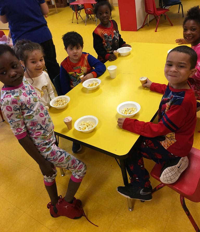 Children sitting at a yellow table with bowls of food