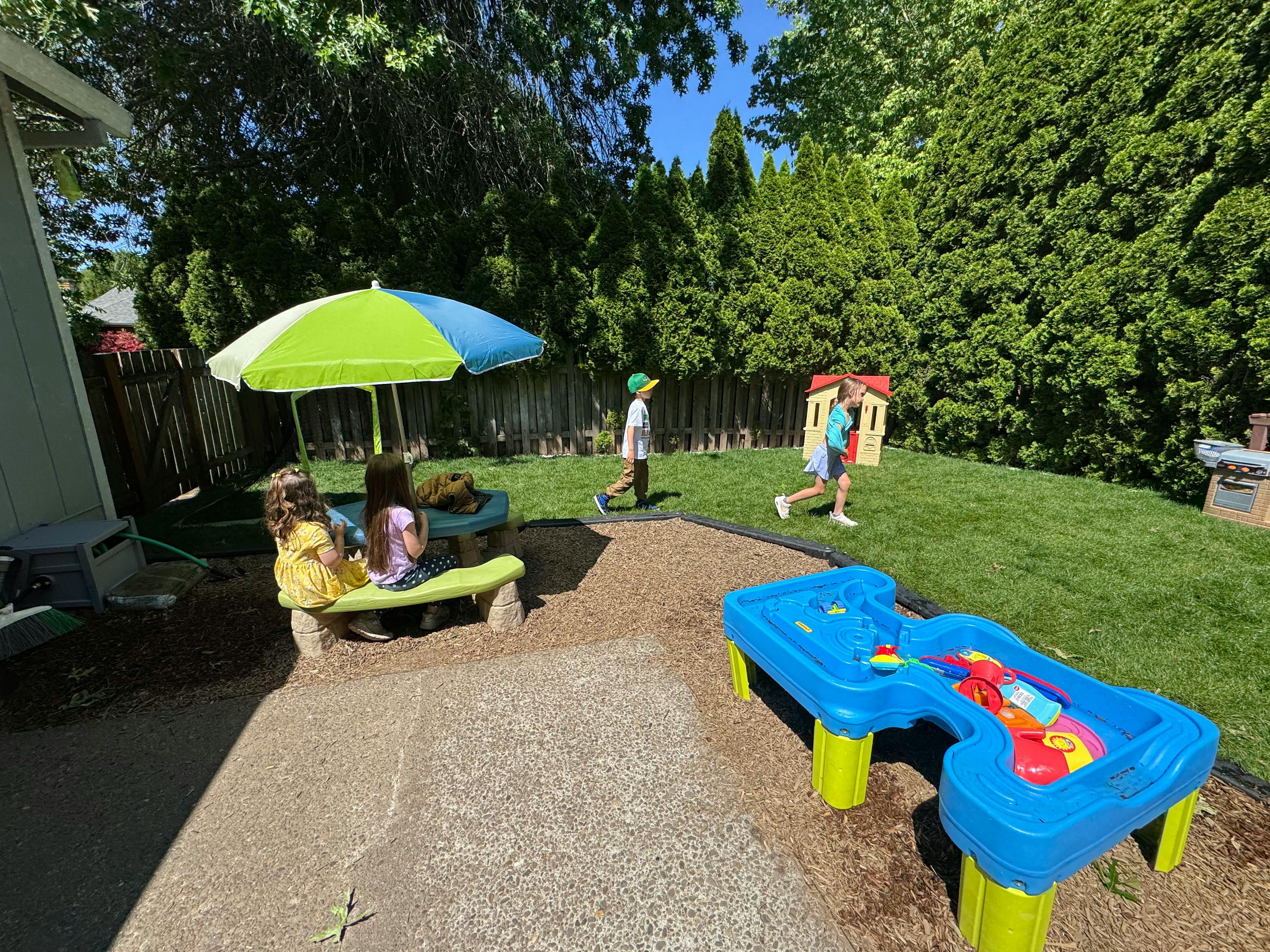 Children playing in a backyard with a sand table and umbrella