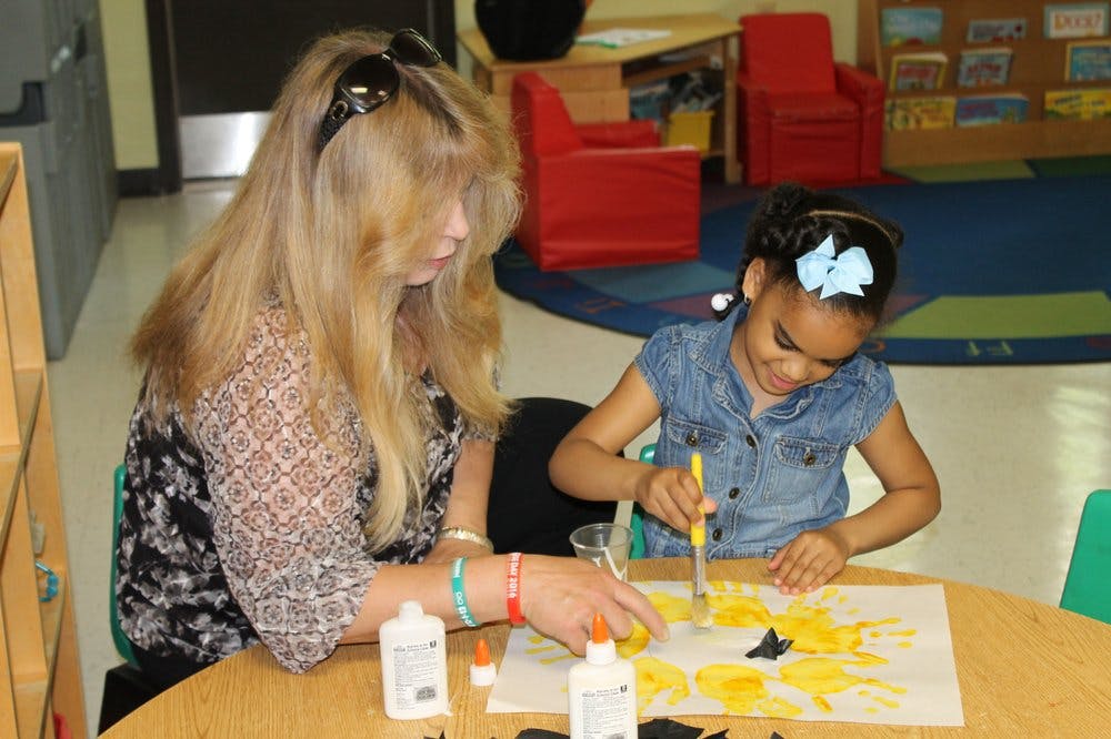 Adult and child doing an art project with glue and yellow paper cutouts